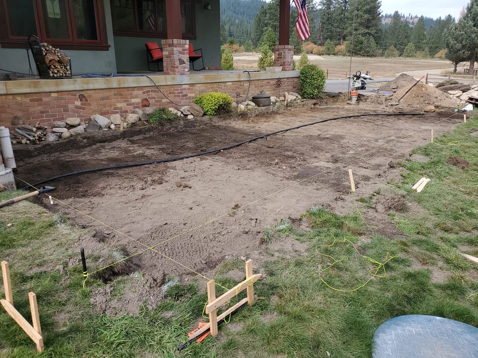 Old patio removed down to bare soil, with string lines and grade stakes set for the new base