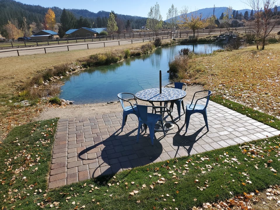 Small paver patio at the pond's edge with a bistro table and four blue chairs