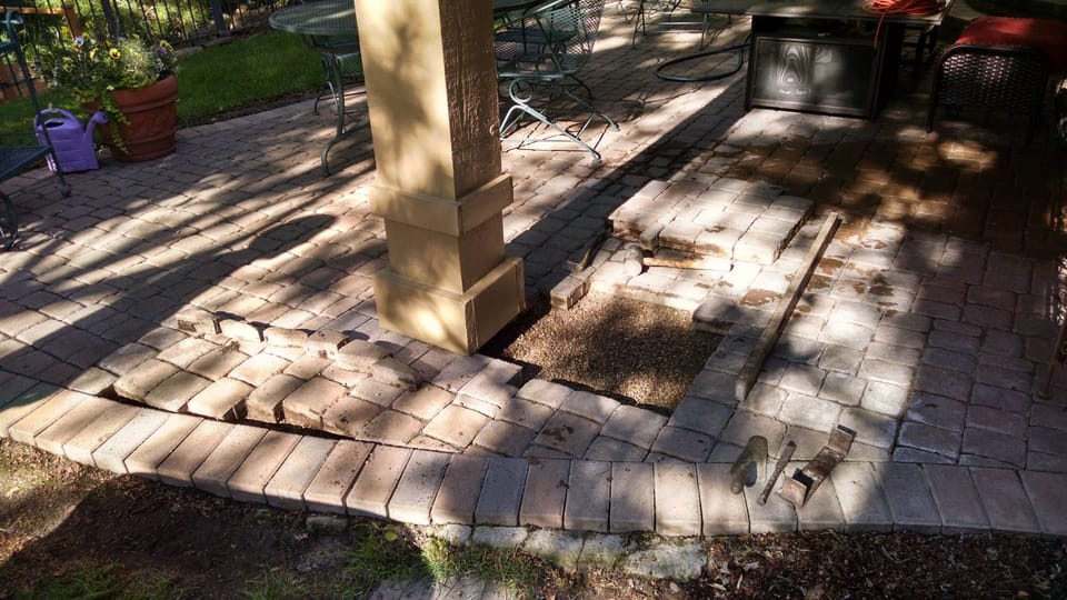 Sunken pavers lifted for repair, exposed gravel base, hammer, chisel and level laid on the patio