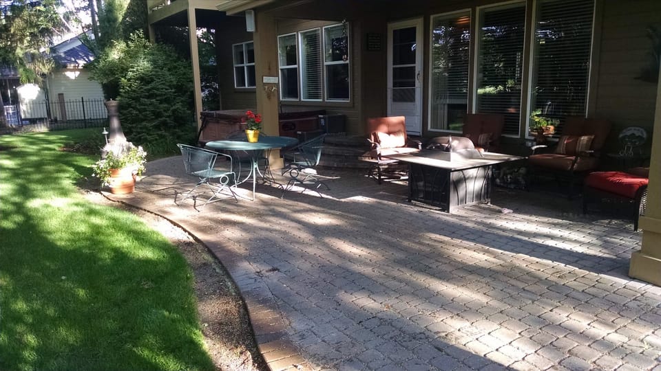 Faded paver patio with sun-dulled color, patio furniture and a fire table beside a covered porch