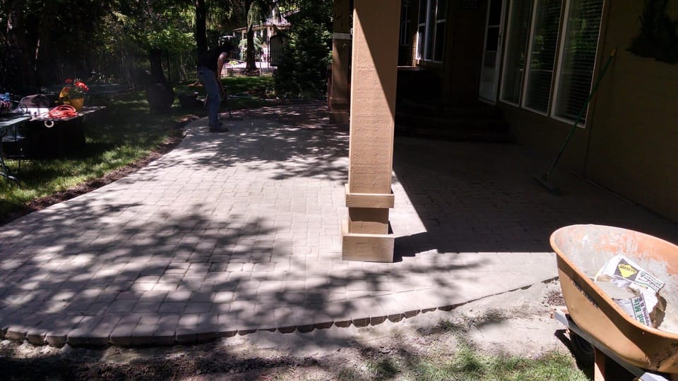 Cleaned paver patio being swept and re-sanded, wheelbarrow of sand-cement joint filler at the edge