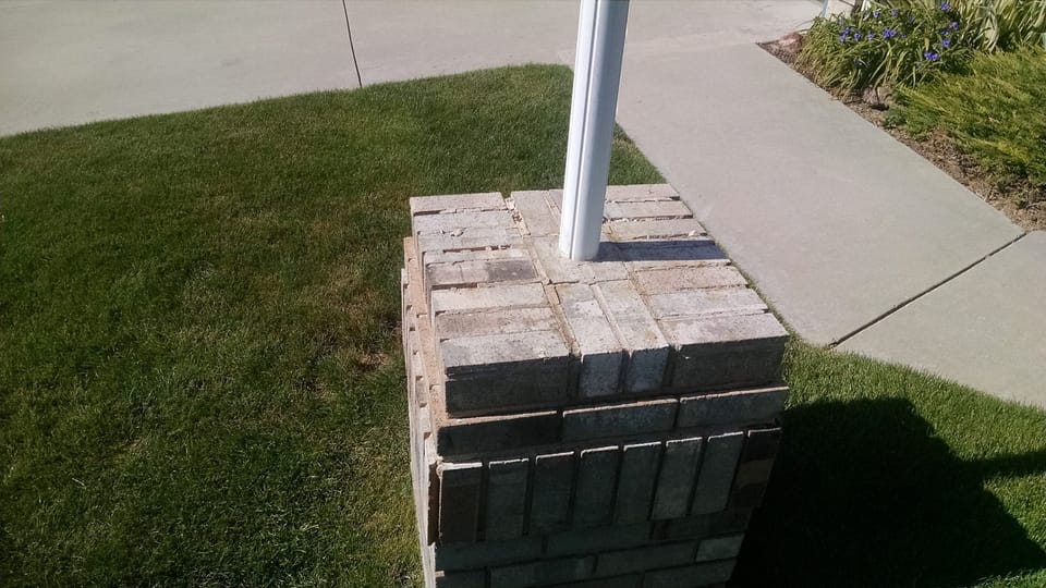 Top of a brick light post with worn, crumbling mortar joints beside a front walk and lawn