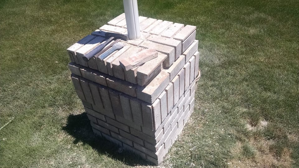Brick light post with cap bricks lifted loose and a mason's hammer and chisel resting on top