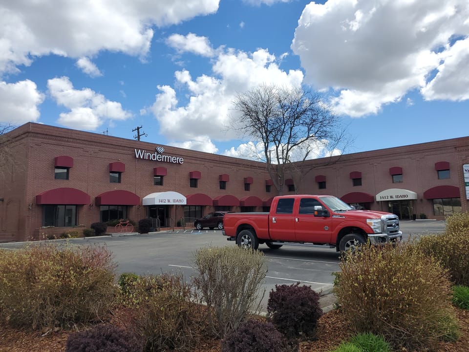Two-story red brick commercial building with maroon awnings and a red pickup in the parking lot