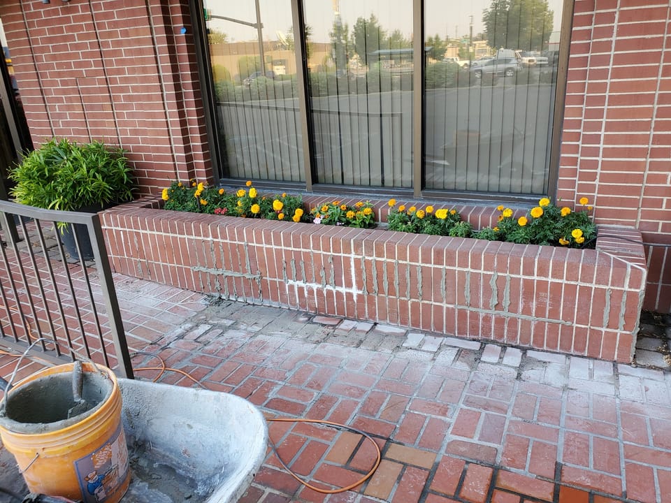 Fresh gray mortar packed into the raked joints of a brick planter wall before tooling