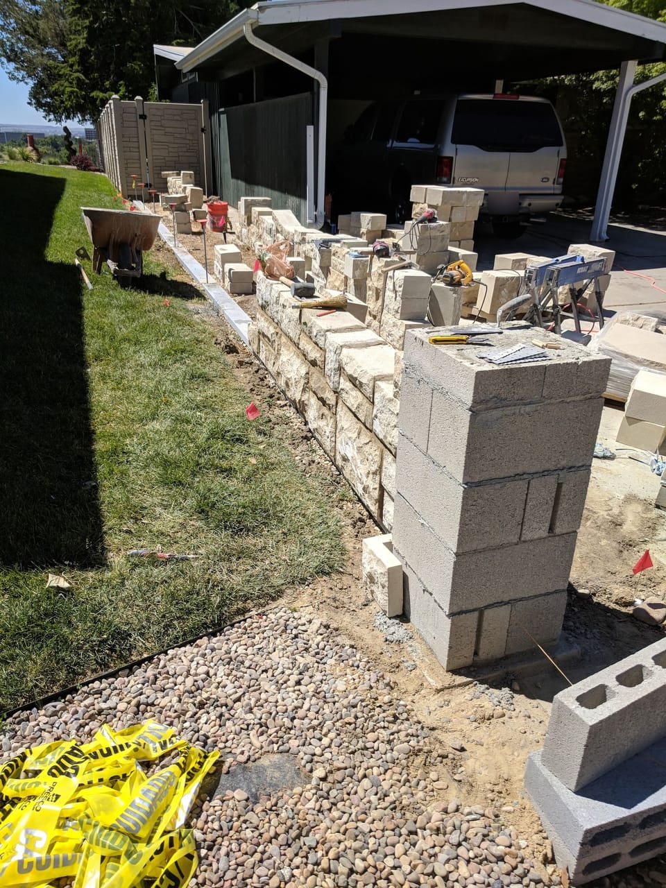 Sandstone fence wall part-built along a driveway with a concrete block pillar core and stone stacked ready