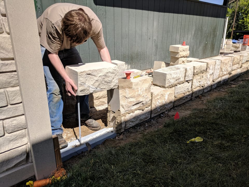 Setting a heavy cut sandstone block onto a mortared wall course over vertical rebar
