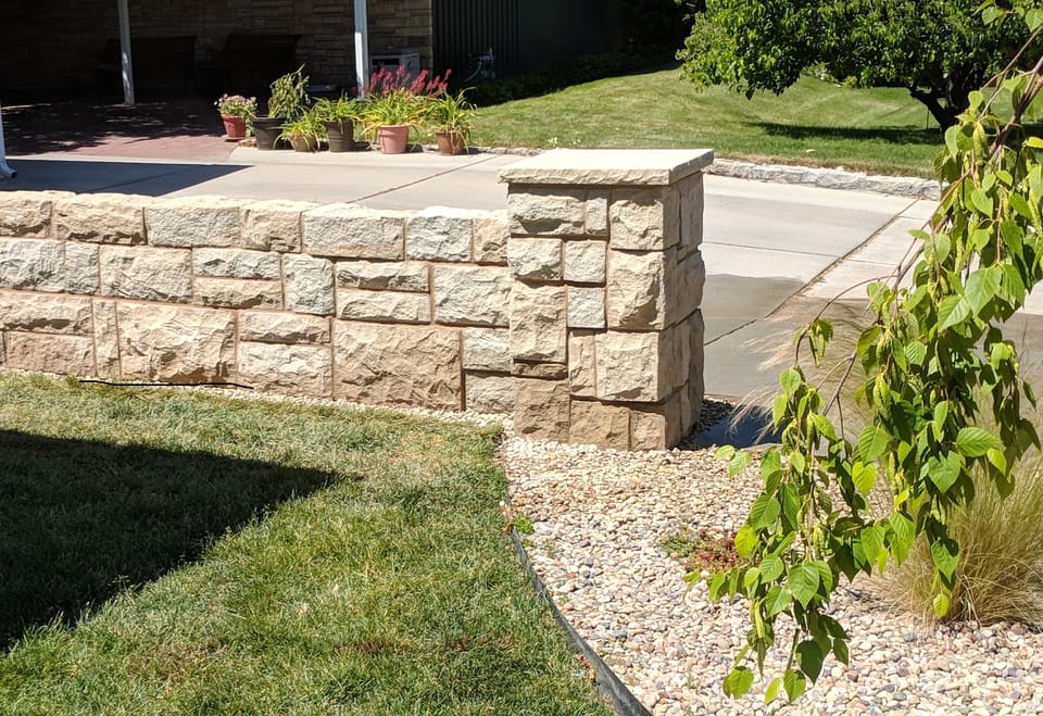 Finished cut sandstone fence wall and capped sandstone pillar edging a driveway and lawn