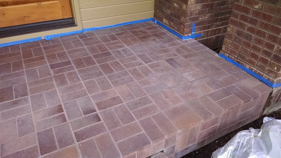 Acid-cleaned brick porch masked off with painter's tape, stains gone and the paver surface etched dull