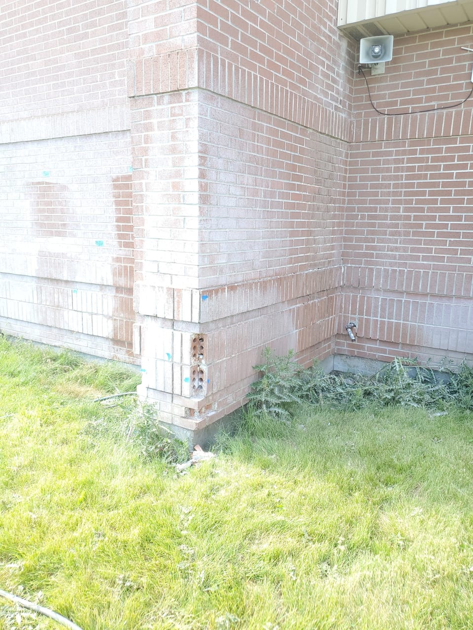 Brick at the base of a Swan Valley School corner with faces spalled off, exposing hollow cores