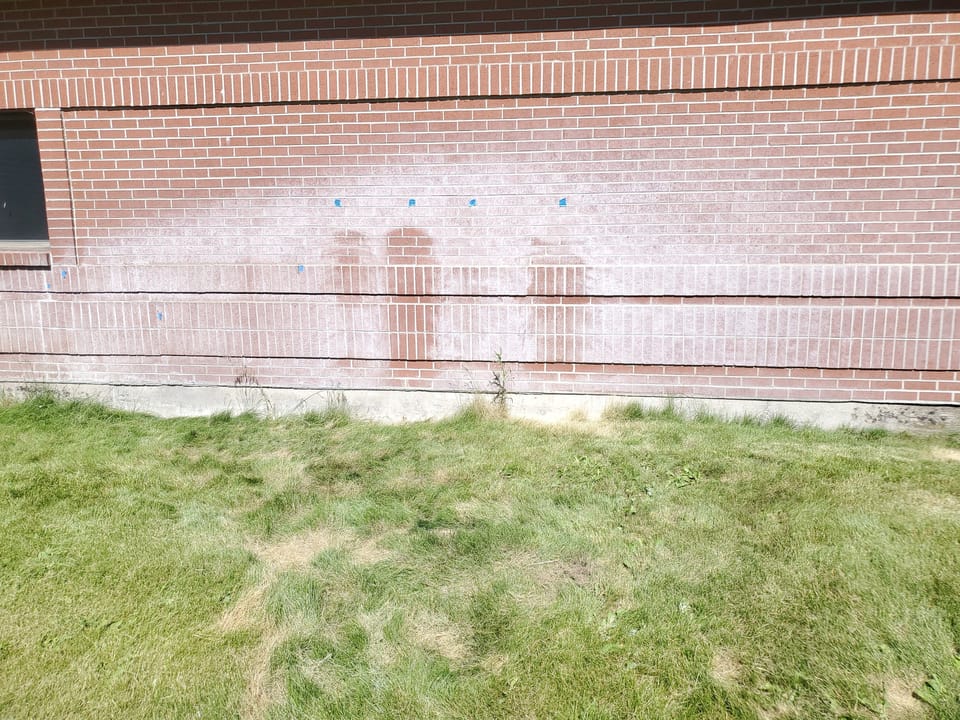 Cleaning test patches and blue tape markers on the stained brick wall at Swan Valley School