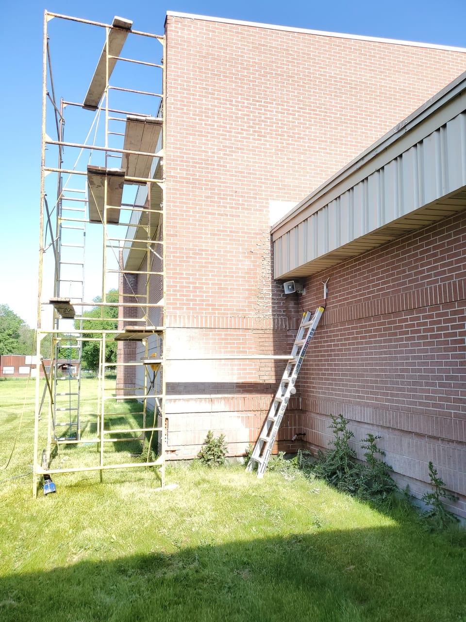 Scaffold tower and extension ladder set against the tall brick gym wall at Swan Valley School