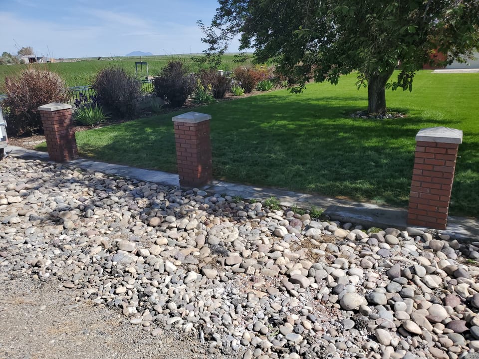 Three rebuilt brick fence posts with concrete caps along a farmyard walk in Arco, Idaho