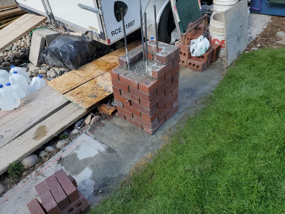 Brick fence post rebuilt partway around rebar and grouted cores, brick and tools stacked nearby, Arco, Idaho