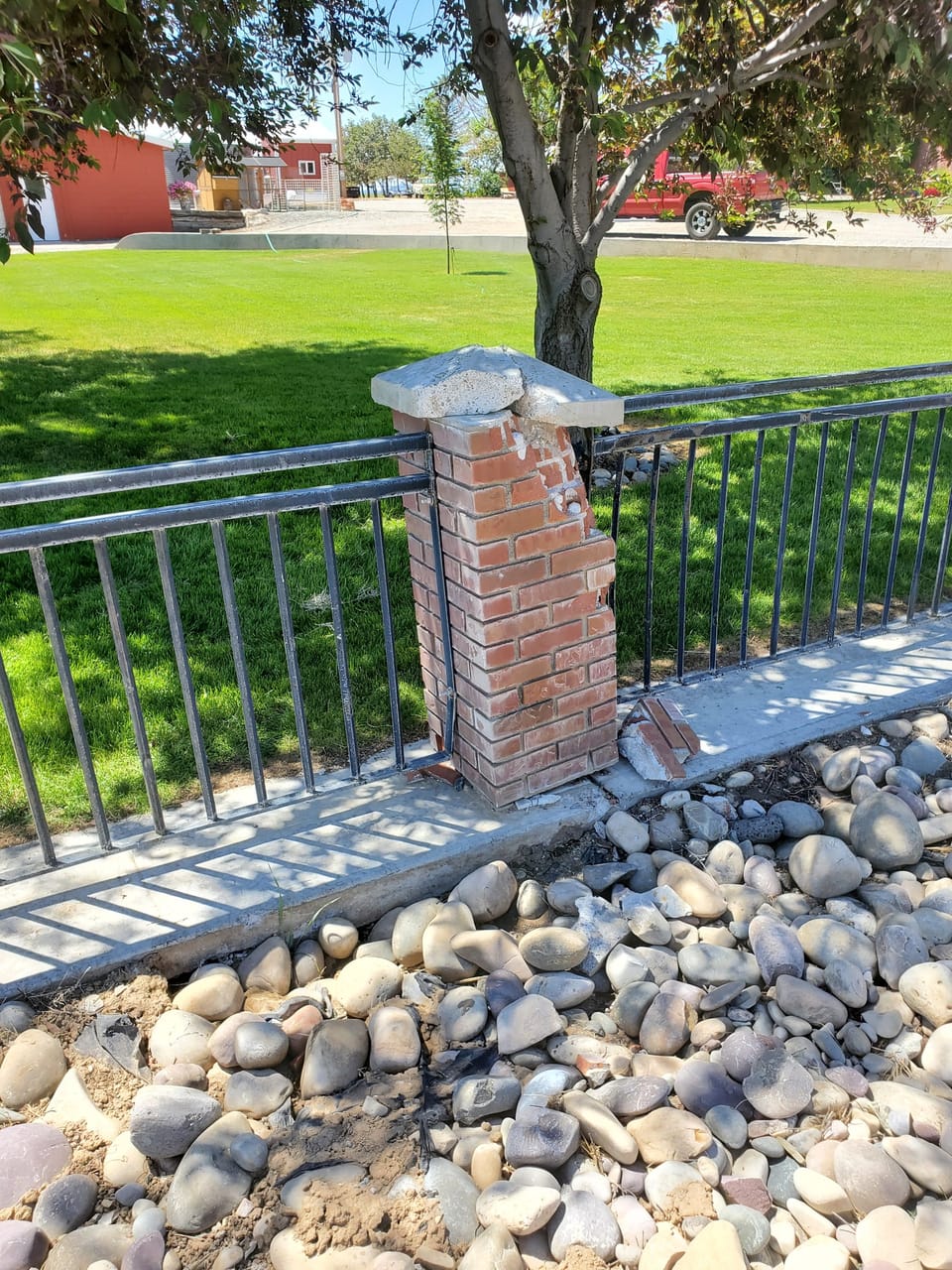Cracked brick fence post with a shifted concrete cap and bent iron railing in Arco, Idaho